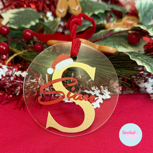 Decorative Christmas ornament with a letter 'S' wearing a Santa hat on a red background.