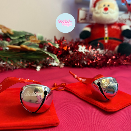Silver bells with 'Believe' text on a red cloth, Christmas decorations in the background